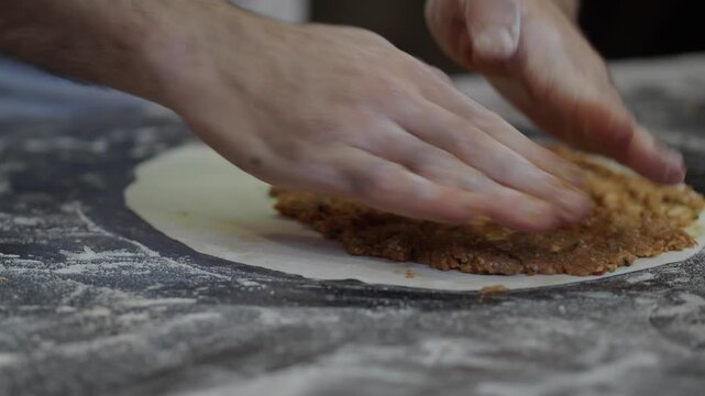 Hands spreading spicy minced meat on thin dough for traditional turkish lahmacun flatbread.