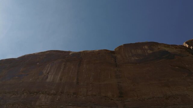 Red sandstone butte near Moab Utah USA, with vertical cliffs of Wingate Sandstone formed by ancient desert dunes in Colorado Plateau, tilt down shot revealing stratification and erosion patterns