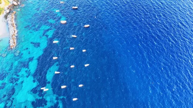 Boats gently sway in clear blue waters of a serene coastal bay at midday under a bright sunlit sky