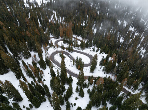 Aerial view of the winding Strada a serpente Passo Giau through a snowy evergreen forest with a car on the road in Cortina d'Ampezzo, Veneto, Italy.