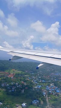 Aerial vertical view from airplane window of wing over tropical island and blue ocean