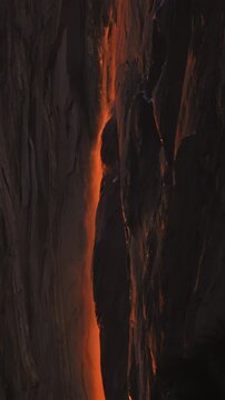Vertical Screen: Yosemite National Park Firefall phenomenon with glowing orange water cascading down granite cliff face at sunset creating stunning natural lava-like effect