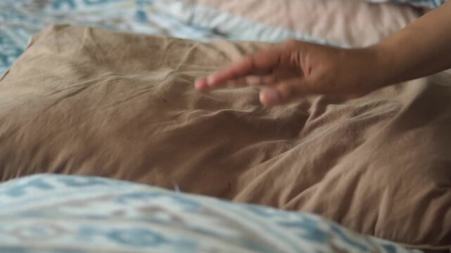 Person adjusts pillow on bed with patterned duvet slow motion comfort and relaxation.