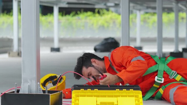 Solar panel technician injured on rooftop lying in pain near toolbox and electrical cable, construction worker accident during maintenance of solar cell system, workplace hazard and safety risk.