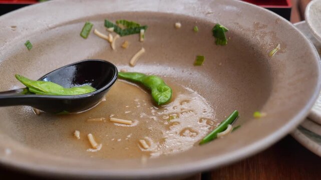 Empty ramen bowl with leftover broth and noodles in close up at japanese restaurant table.