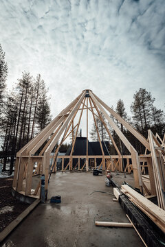 Wooden house frame under construction in forest with cloudy sky