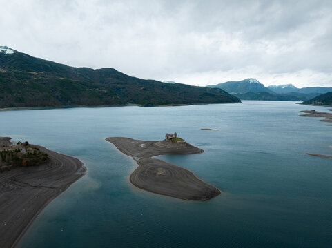 Aerial view of Lac de Serre-Poncon featuring the Saint-Michel chapel on a small island surrounded by receding water and mountain peaks Provence-Alpes-Cote d'Azur, France.