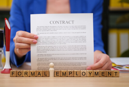 In a vibrant office setting, a person holds a contract titled Contract while a small wooden figure sits in front of them. The scene symbolizes new beginnings and formal employment opportunities.