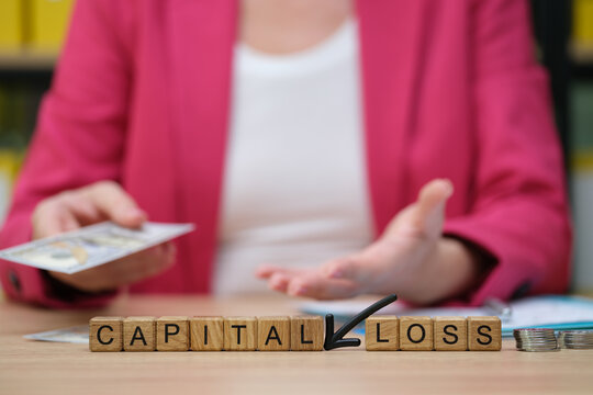 A businesswoman in a pink blazer holds financial documents, expressing concern about capital loss. She sits at a wooden desk, emphasizing important decisions in a bright office setting.