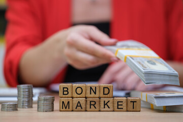 In a lively office setting, a person in a red blouse is handling cash while wooden blocks spell out...