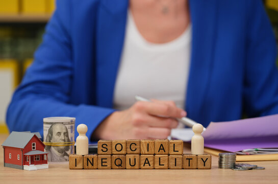 Colorful wooden blocks spell out social inequality during a thoughtful discussion in a lively academic setting. Nearby, miniature models and money inspire deep conversations about societal issues.