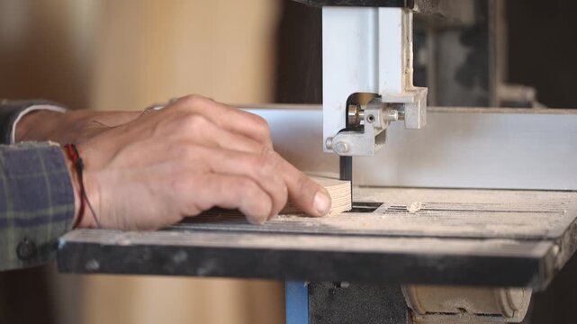 Close up of hands cutting wood on scroll saw in workshop. Precise carpentry process with fine detail, ideal for craftsmanship, woodworking, DIY and artisan themes.
