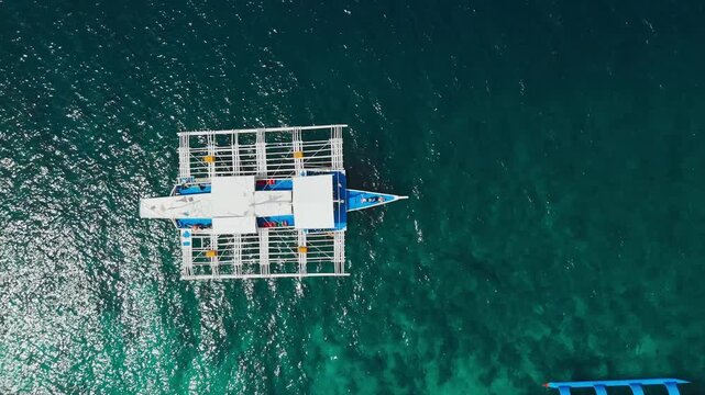 Drone shot of catamaran boat in the pacific ocean with a couple sunbathing at the front. 