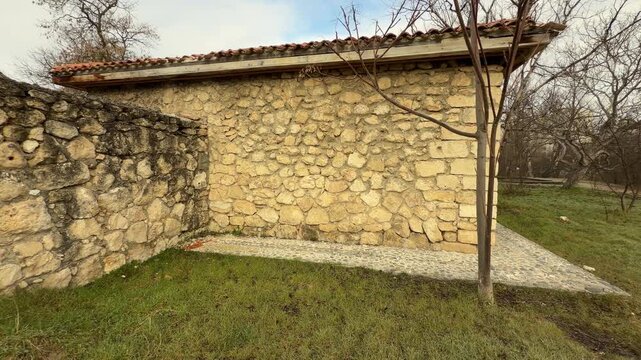 A long stone building with a red tiled roof stands on a grassy field. The rough walls and bare trees create a calm, nostalgic feeling. This peaceful scene captures the quiet beauty of a cold morning.