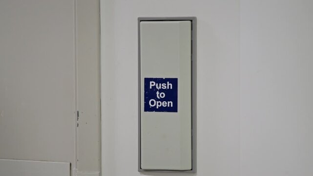 Close-up of a hand pressing a &ldquo;Push to Open&rdquo; button on a wall-mounted door release panel in a hospital. The image highlights accessibility features in healthcare environments.