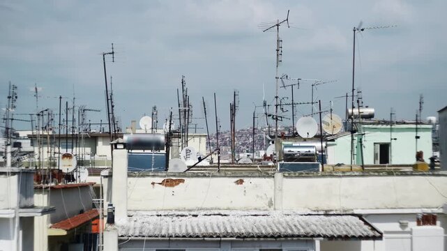 A dense array of antennas and satellite dishes atop urban rooftops with a city view. Ideal for scenes depicting telecommunications or urban density.
