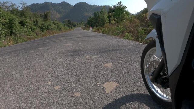 Low to ground angle of a scooter front wheel as it is ridden around Laos with nobody else in sight.