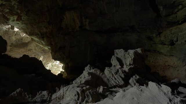 Slow pan across the interior of Xieng Liap cave in Laos. Lit up from the left, off screen cave entrance and another entrance in the distance.