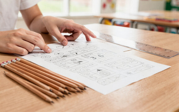 teacher hands pointing at worksheet beside pencils and ruler classroo
