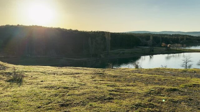 Bright sunlight glows over a calm lake and rolling green fields. This scenic view feels serene and deeply refreshing. The warm morning light creates a hopeful and quiet atmosphere.