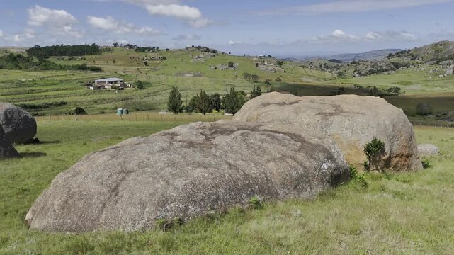 Drone orbits to right over grassy field with large boulders on a sunny day at Sibebe Rock near Mbabane, Eswatini