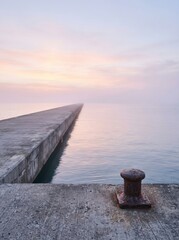 Fototapeta premium Minimalist view of an empty concrete pier at dawn with a mooring bollard. Peaceful maritime landscape representing potential, space, and the quiet side of harbor logistics.