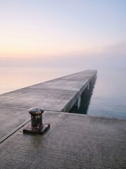 Fototapeta premium Minimalist view of an empty concrete pier at dawn with a mooring bollard. Peaceful maritime landscape representing potential, space, and the quiet side of harbor logistics.