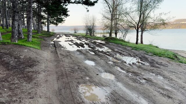 Large puddles of water sit in deep ruts on a messy dirt path by a quiet lake. This rugged scene creates a lonely and melancholic feeling of a cold, damp day in the wilderness.