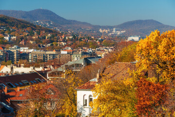 Naklejka premium Breathtaking panoramic view of Budapest Hungary during vibrant autumn season showcasing colorful fall foliage historic architecture and rolling green hills against a bright blue sky