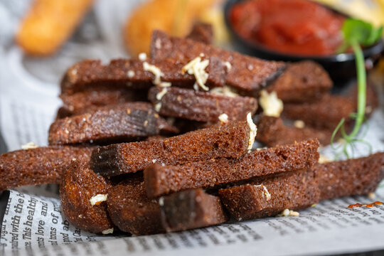 crispy dark rye garlic croutons sprinkled with grated cheese resting on newspaper-style paper