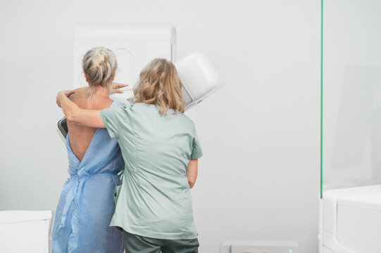 50-year-old woman undergoes mammography procedure on special medical equipment mammograph with help of assistant in modern clinic. Regular medical examination, screening for breast cancer back view