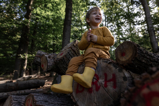 Child in yellow boots smiling on log in autumn forest outdoors