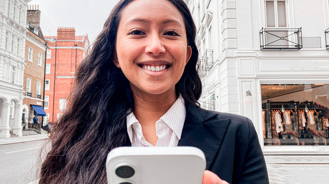 Smiling businesswoman using smartphone outdoors in London street