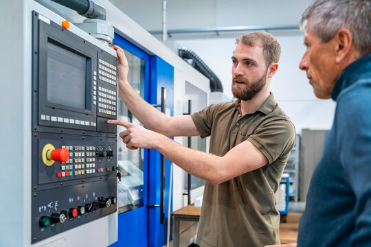 Young engineer explaining machine system to senior colleague in production hall