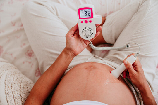 Pregnant woman monitoring fetal heartbeat with doppler at home