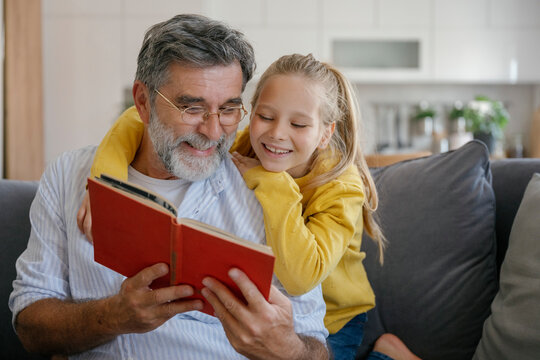 Grandfather and child reading book and hugging on couch indoors