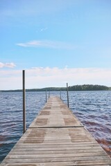 Fototapeta premium Wooden pier on a calm lake under a clear blue sky. Scenic view of a dock stretching into the water with forest on the horizon.