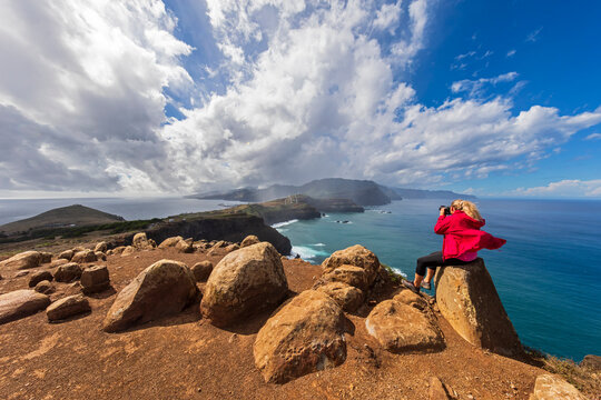 Tourist in red jacket photographing scenic cliff view in Madeira