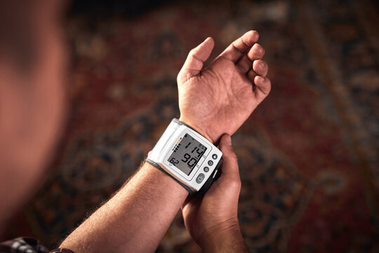 Man checking blood pressure and heart rate at home with a portable modern digital meter.