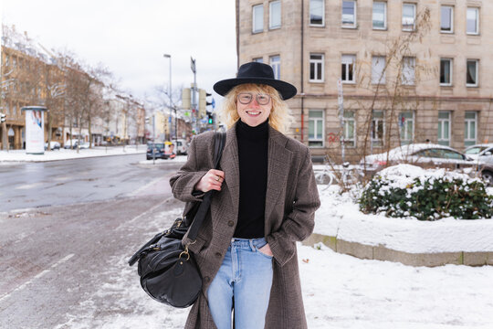 Cheerful young amn walking on snowy city street in stylish winter fashion