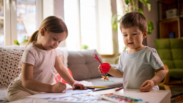 Little children drawing together at table using pencils and paper during creative playtime at home. Concept of collaborative activity, kids education content and family bonding through creativity