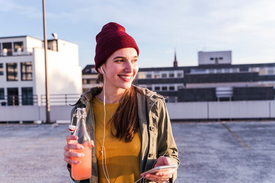 Smiling young woman outdoors with drink and mobile phone in city