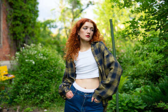 Woman with red curly hair in casual outfit posing outdoors in garden