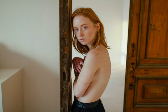 Red haired woman with freckles standing indoors in soft sunlight