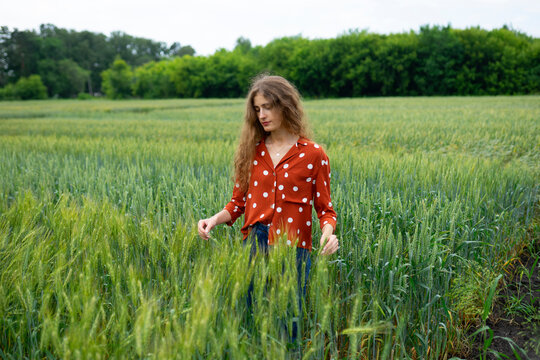 Woman with curly hair in red blouse smiling in wheat field