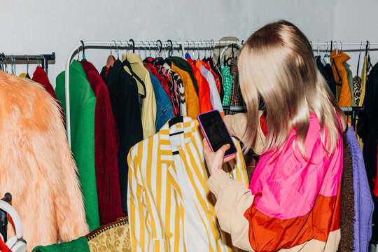 Woman using smartphone to sell stylish clothes online in wardrobe