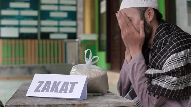 Asian men praying together near zakat sign and rice bag, communal reflection after donation, mosque veranda setting with green