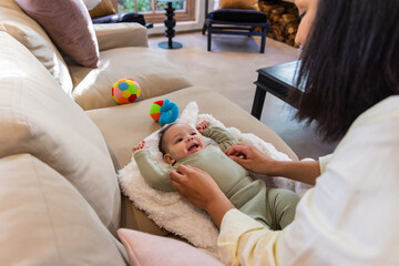 Naklejka premium Female caregiver and infant smiling, adjusting light green knit one-piece on plush blanket on sofa