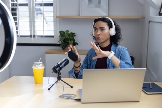 Non-binary adult speaking and gesturing in home studio with denim jacket, white headphones, mic