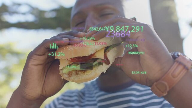 Man sitting under tree eating hamburger, financial charts floating and scaling with each bite